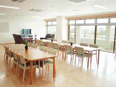 木製のダイニングテーブルが並んだスペースの奥にはブラウンのソファやテレビが設置されたスペースがあり、花も飾られている。