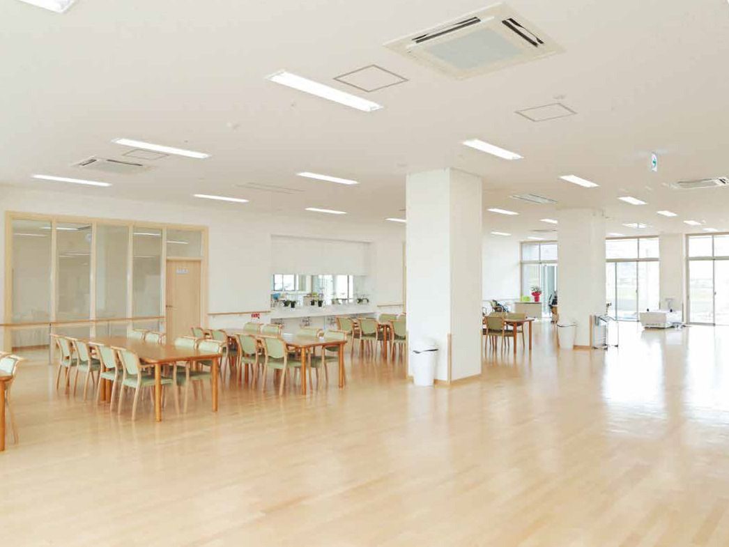 川が流れ、適度な自然が残る環境が魅力的な場所に建っている白を基調とした大きな建物、桜の花も咲いている。