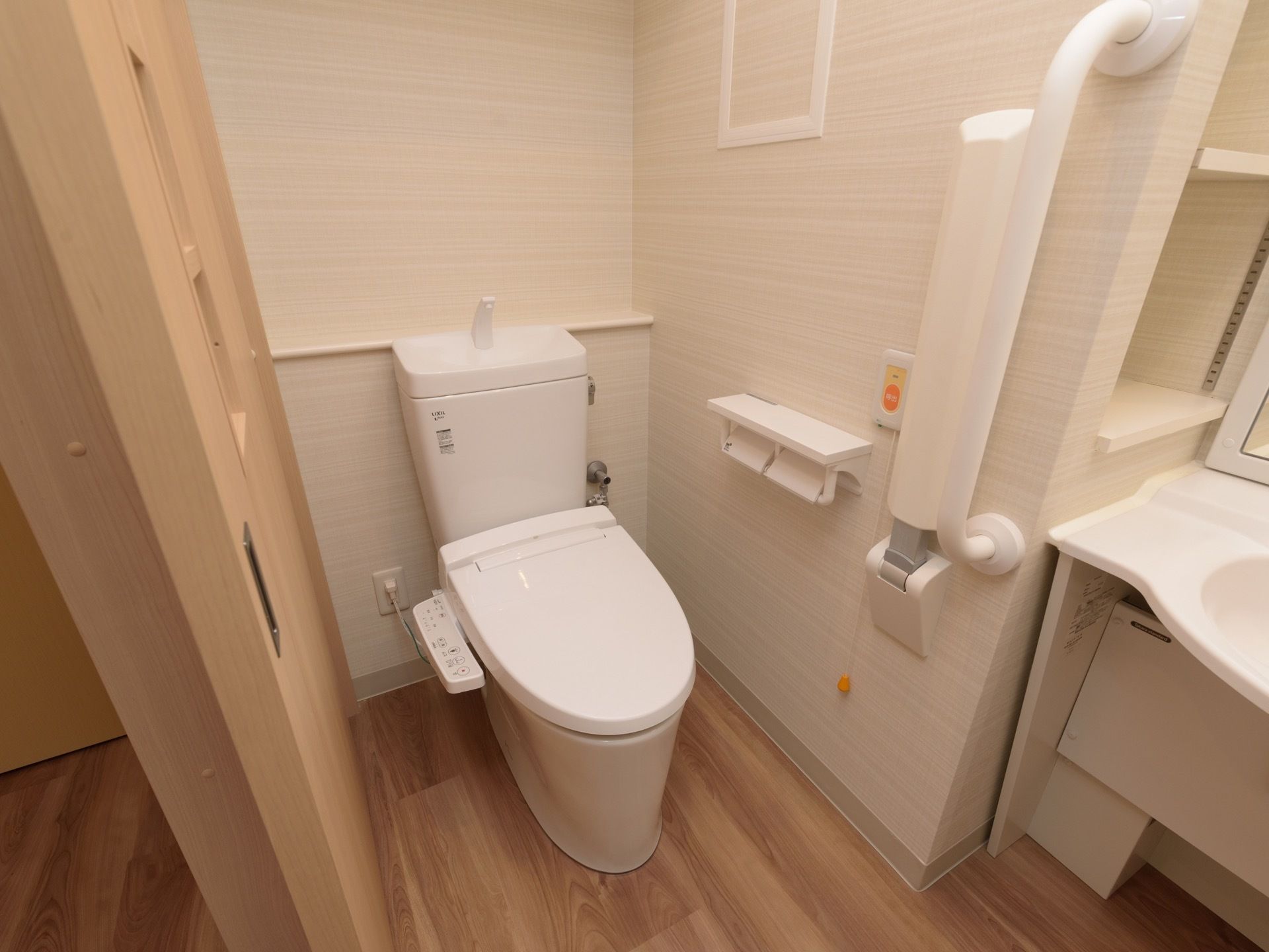 引き戸の入口が左手にあり、中央にトイレがある。便座には温水洗浄便座が取りつけられ、壁に非常ボタンがある。