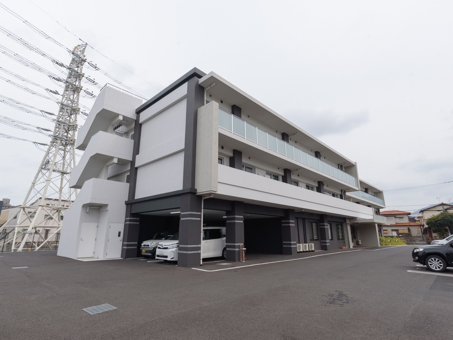 ３階建ての建物で、白とダークグレーに塗り分けられた施設である。１階部分は駐車場になっており、車が停まっている。