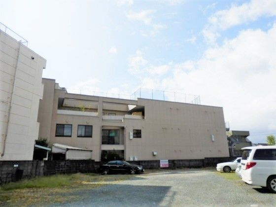 駐車場には複数の車が止まっていて、3階建ての建物には屋上が付いている。
