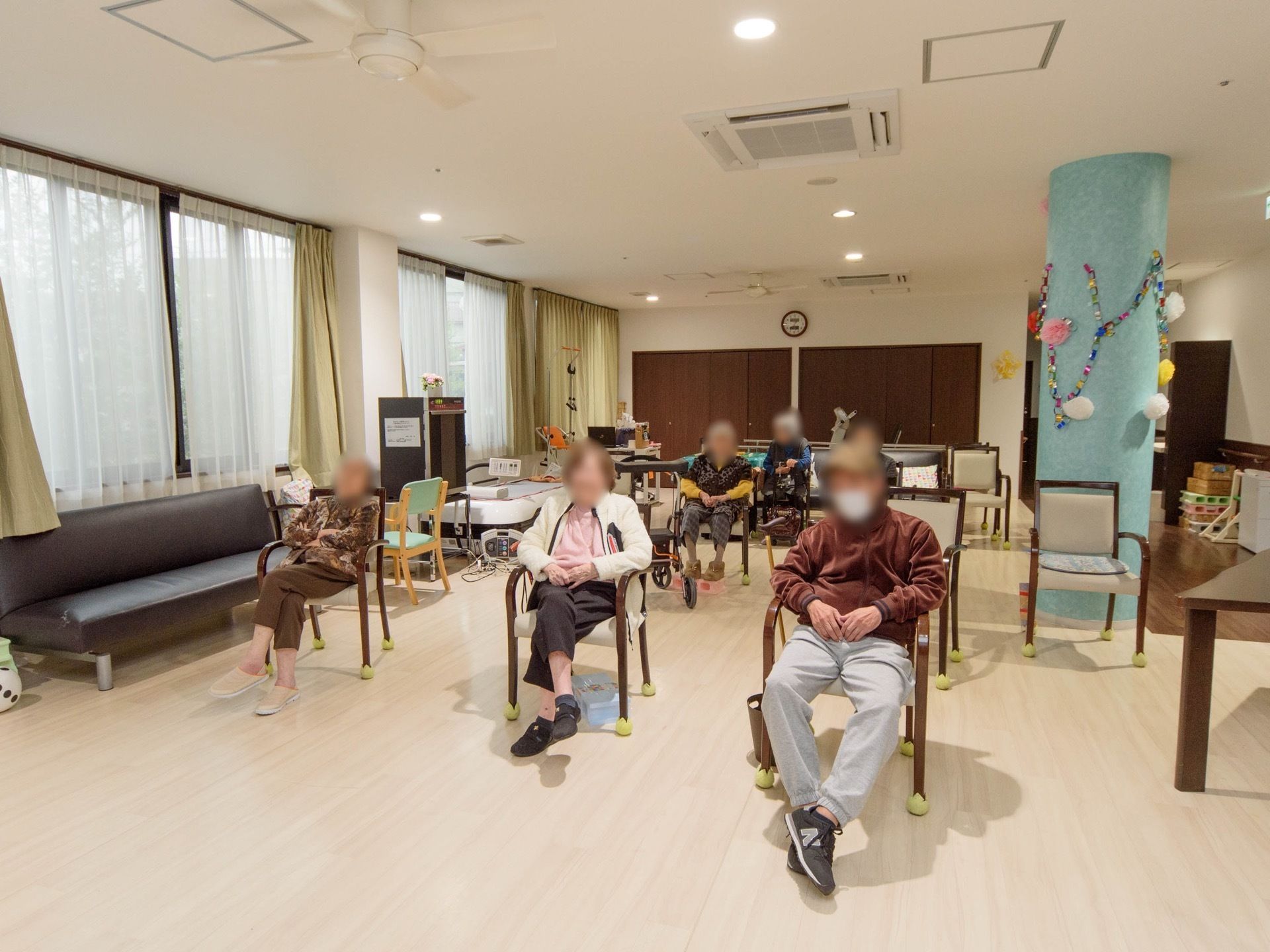 空調設備の整っているフロアで、窓際にはソファーが置かれている。複数の入居者様が、一定の方向を見て椅子に座っている。