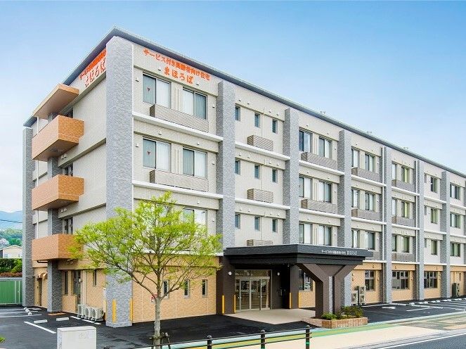 オレンジとグレーの４階建ての建物の周りには草木も植えられ、駐車場もあり、玄関には車寄せが付いている。