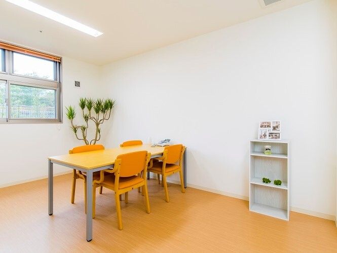 ４人掛けのテーブルセットが置かれた部屋には棚や観葉植物があり、窓も付いている。明るい雰囲気。