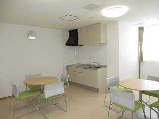 IHクッキングヒーター付きのキッチンが設置されたリビングダイニング。テーブルセットが複数置かれている。