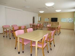 テレビが設置された共有スペースにはピンクの椅子がセットされた木製のダイニングテーブルが複数置かれている。