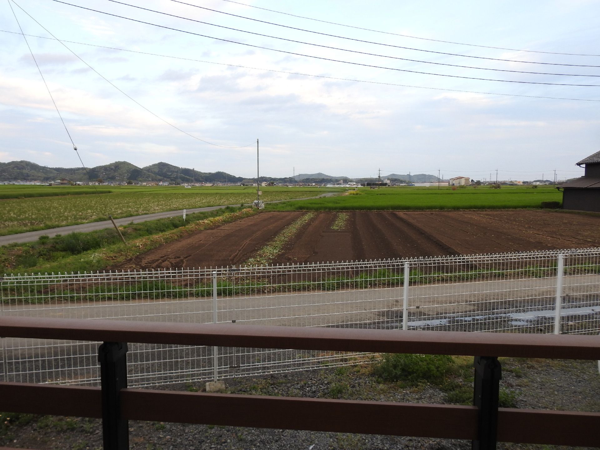 ホームの目の間にはよく手入れの行き届いた畑が広がっていて、周りには緑が多い。奥には民家があり、山々も連なっている。