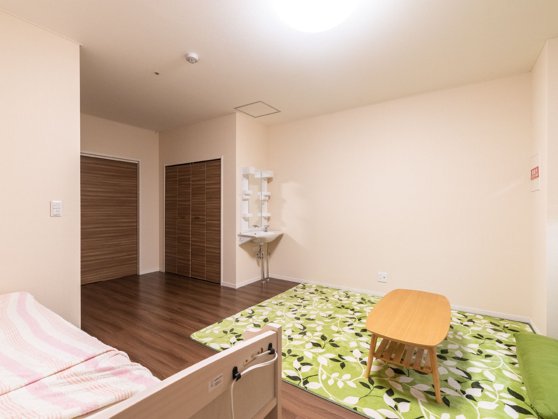 ベッドと木製の机が置かれた白い壁の部屋
