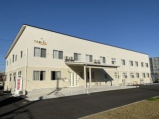 淡いベージュの2階建ての建物は駐車場や自動販売機もあり、玄関には大きな屋根が付いている。