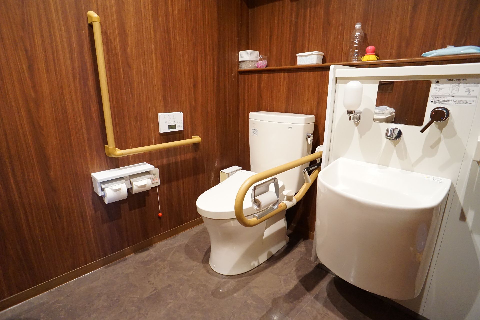 茶色い壁に並んだ木製の手すりに囲まれた洋式便器とオストメイトパック