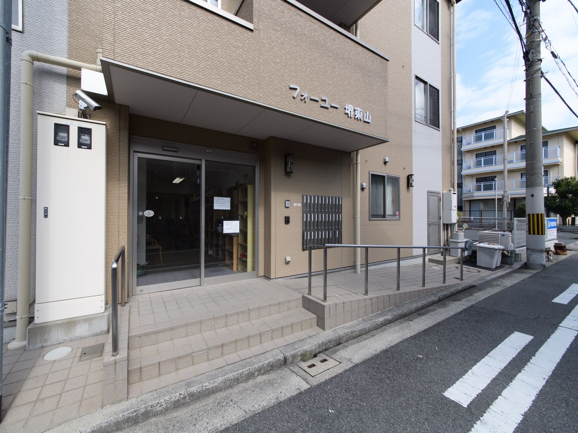道路に面して立地している施設の外観。ブラウンを基調とした落ち着いた雰囲気になっている。道路から玄関まで、階段とスロープが設置されている。