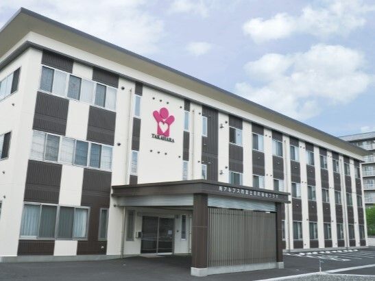 白と黒の外壁の３階建ての建物の玄関には車寄せが付き、敷地内には広い駐車場がある。