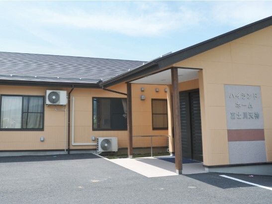 グレーの瓦屋根が付いた平屋建ての建物の外壁はベージュで、日当たりのいい場所に建っている。