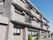 グレー系の３階建ての建物は各フロアにベランダがあり、日当たりも良好。低木も植えられている。