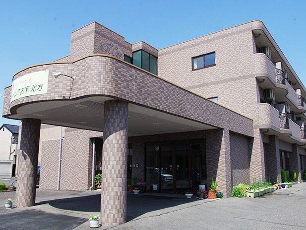 グレー系の３階建ての建物は大きな車寄せが玄関に付いていて、建物の周辺にはプランターが多く置かれている。