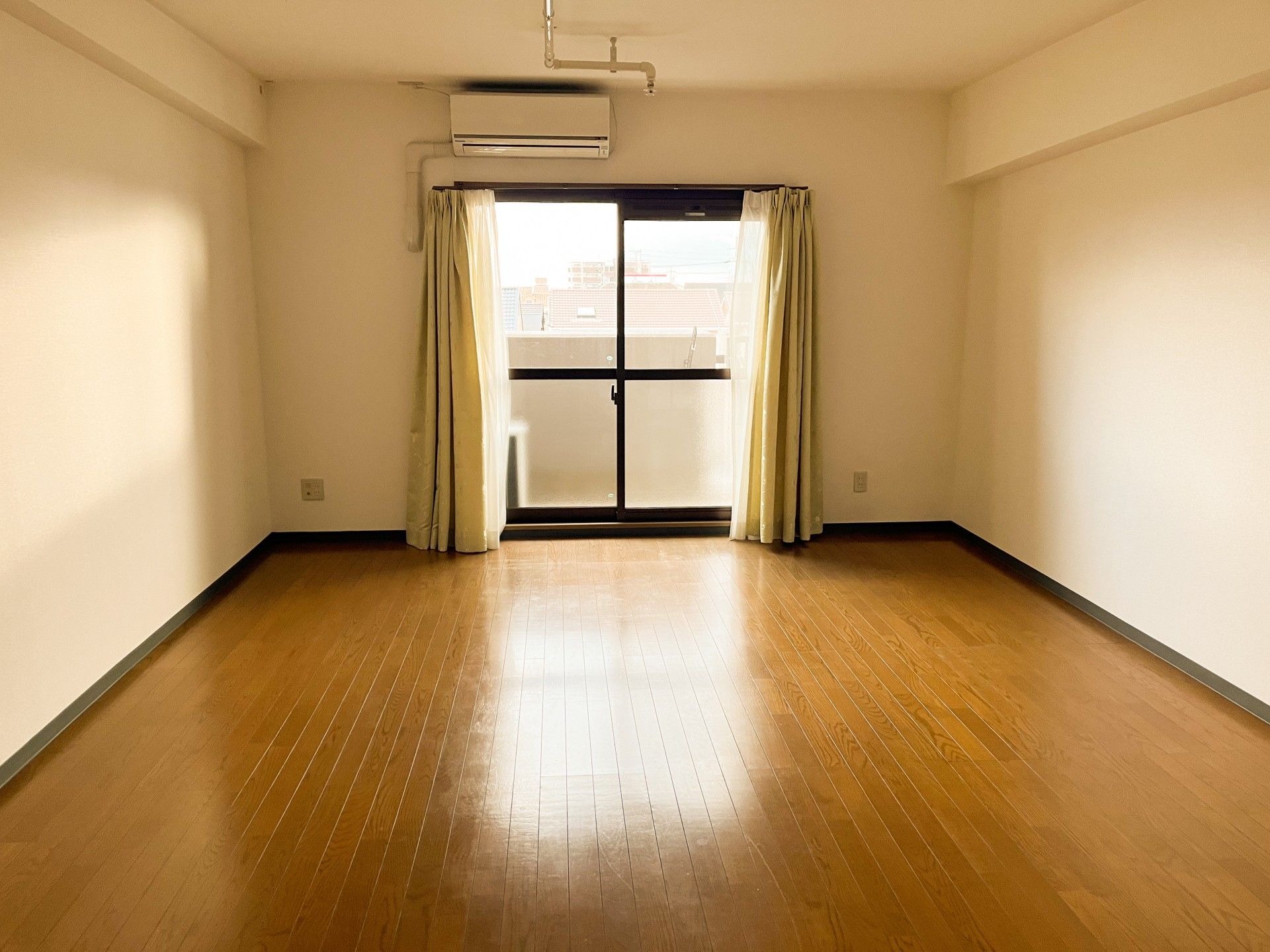 エアコンが付いたフローリングの部屋には大小の窓があり、ピンクのカーテンが付いている。