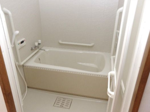 白でまとめられた浴室には一人用の浴槽が設置され、壁には手すりやシャワーが付いている。