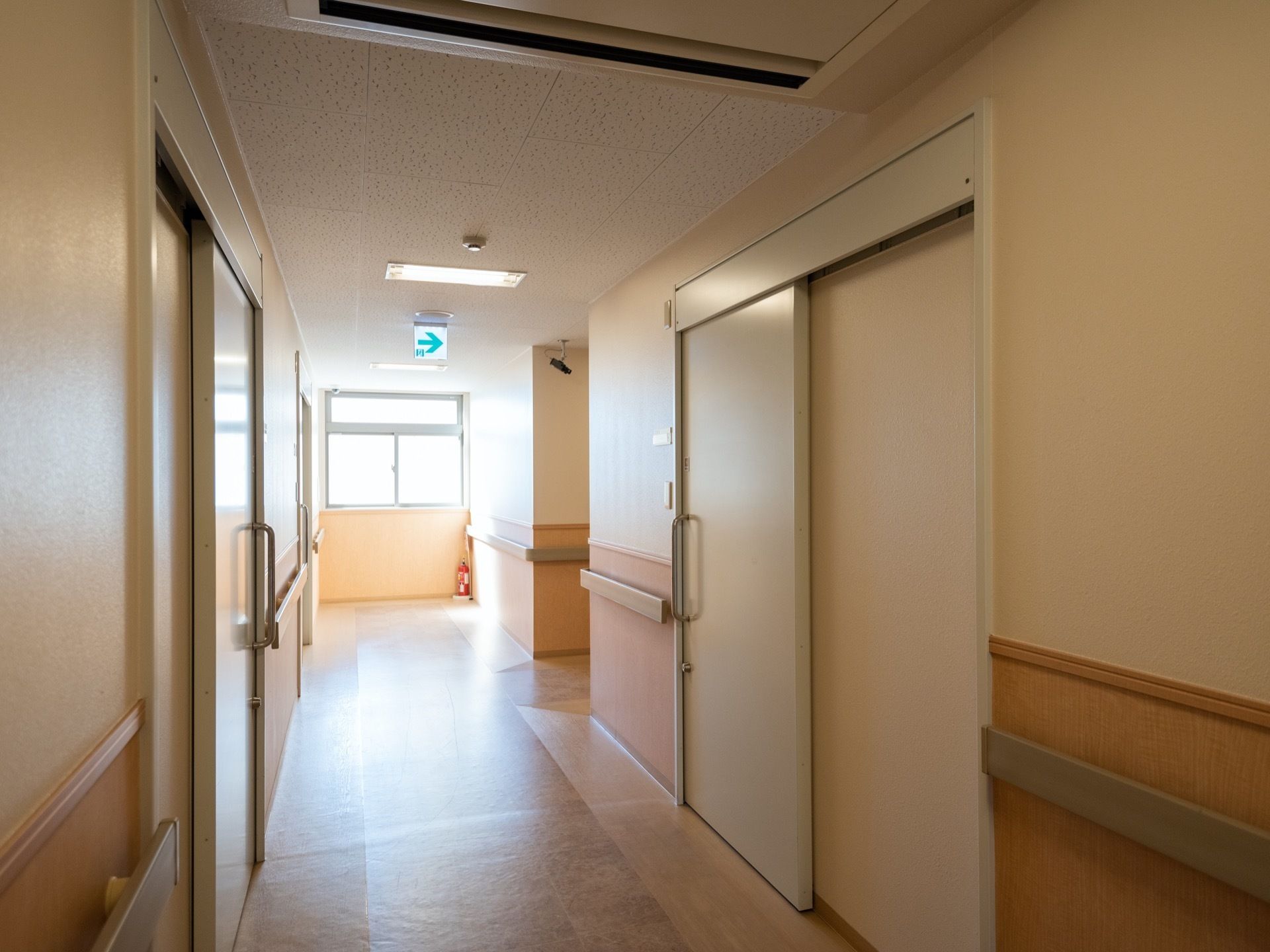 突き当たりの窓から陽光が差し込んでいる明るい通路である。両側の壁には、にぎりやすい手すりが完備されている。
