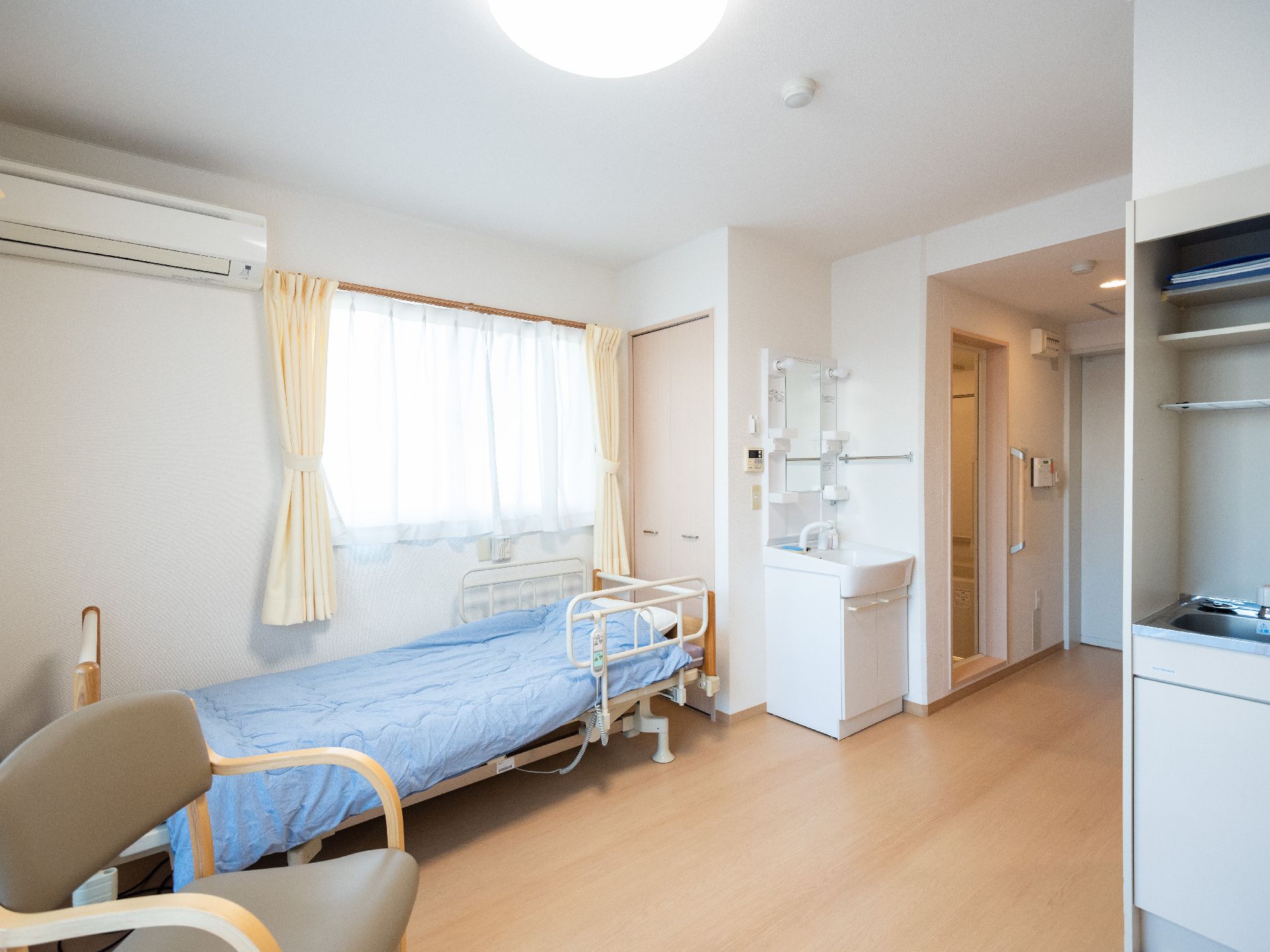 ベッドと椅子が置かれている、洗面台やエアコンがある部屋