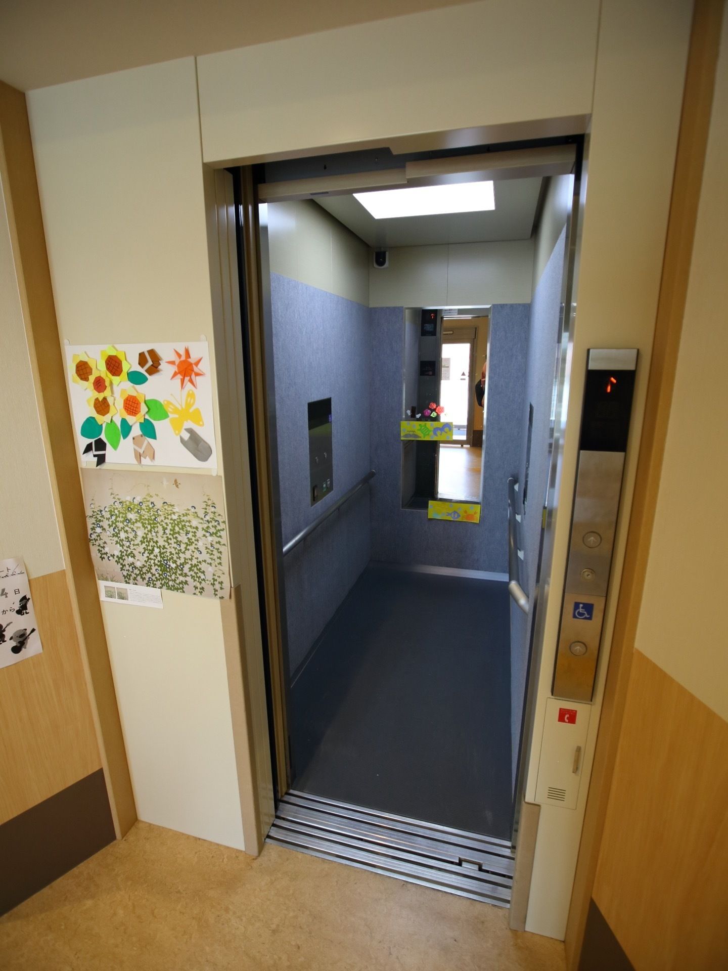 エレベーターには車椅子専用ボタンが設けられている。エレベーター内やエレベーター横の壁には折り紙で作られた掲示物が飾られている。