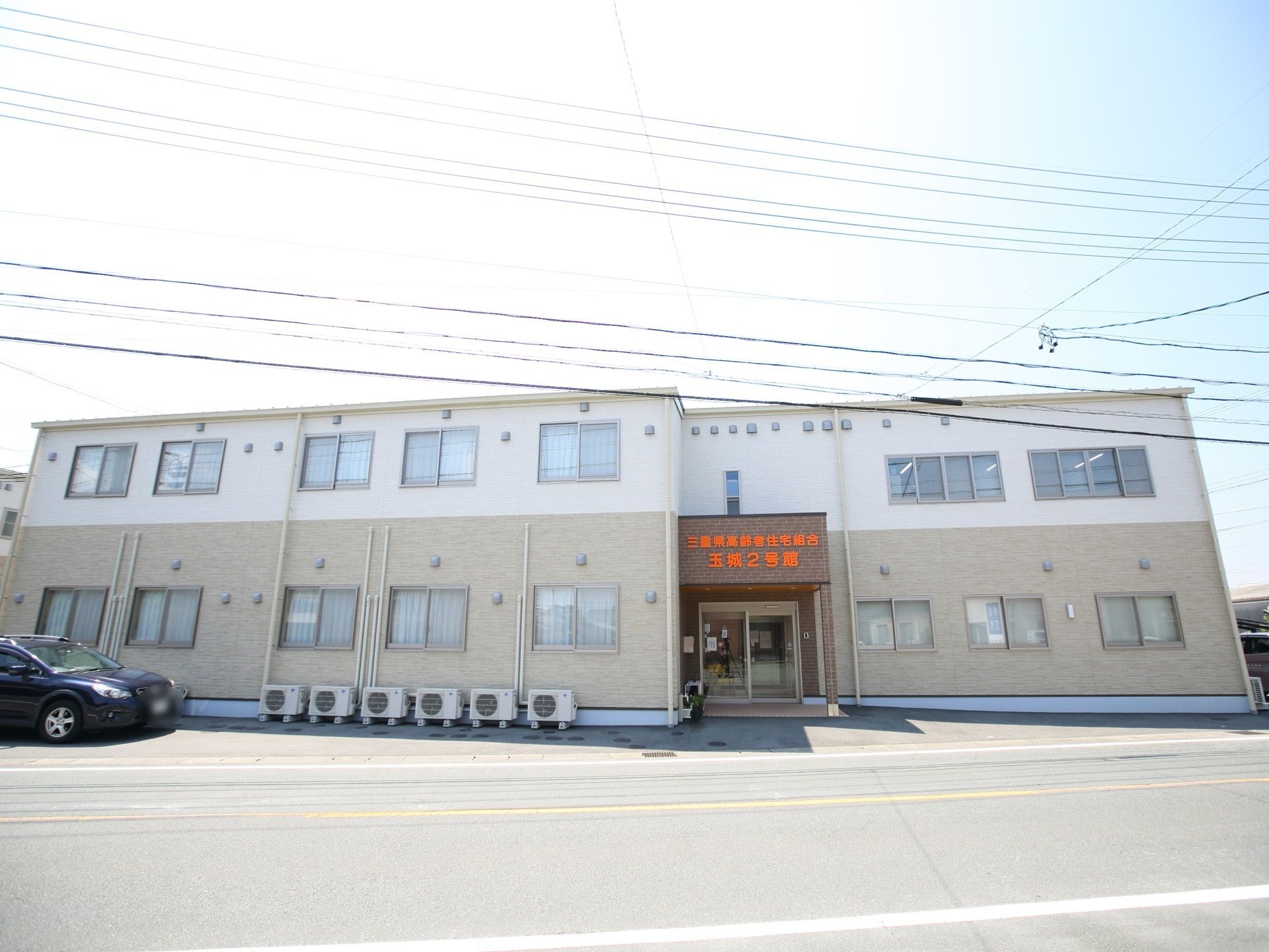 二階建ての建物が見える。一階と二階部分で外壁材が貼り分けられている。ひさしには施設名が書かれている。