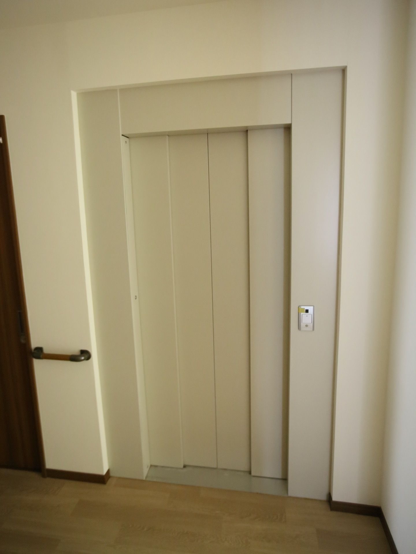 ドアの色は白色。エレベーター内部と外部との間に、段差がない。エレベーター脇に手すりが、設置されている。