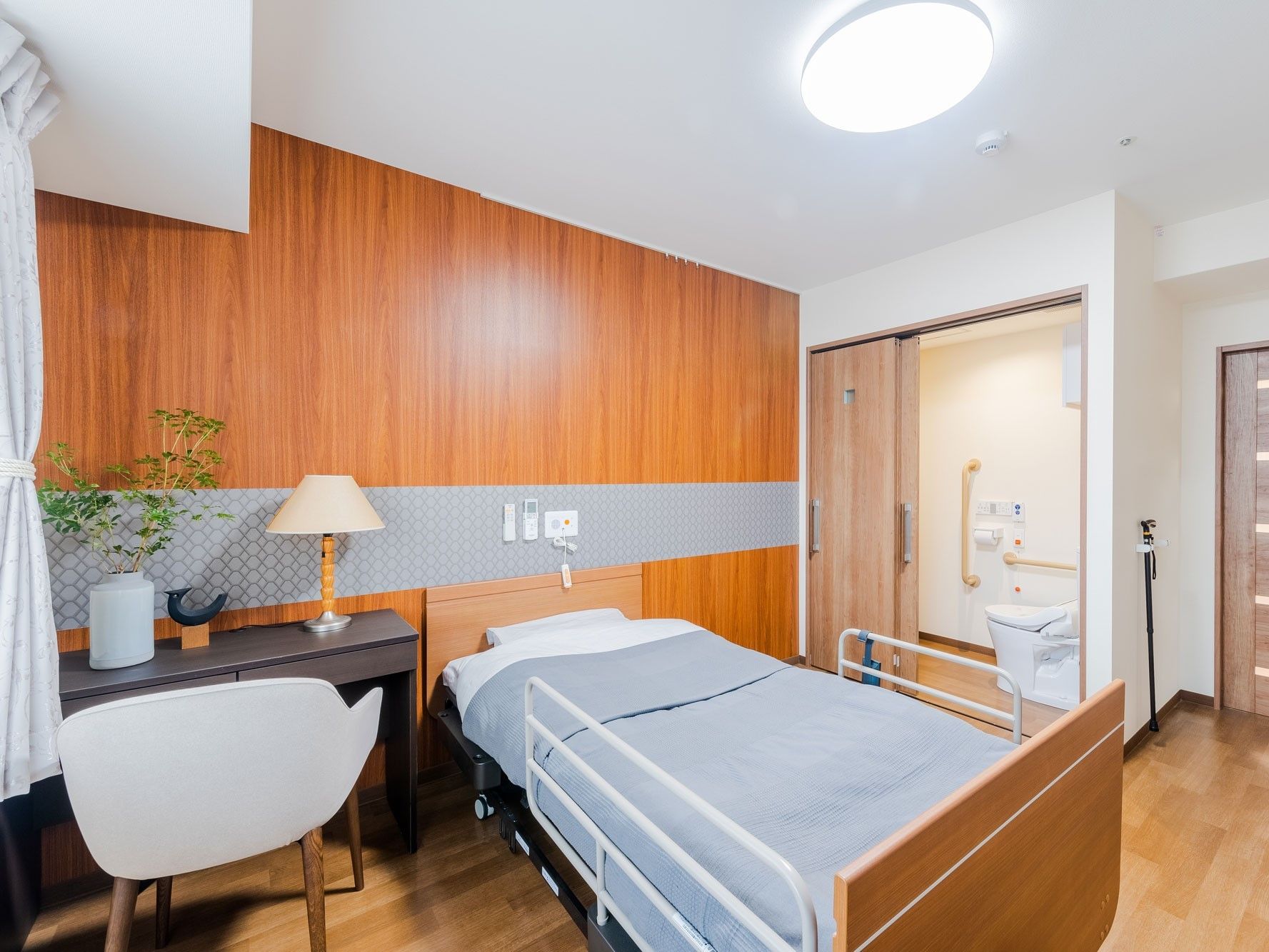 寝具がセットされたベッドが置かれたフローリングの部屋には、テーブルセットやトイレもある。
