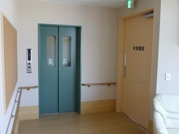 手すりが設置された館内にはグリーンの扉が付いたエレベーターがあり、その横には「非常用階段」と書かれた扉がある。
