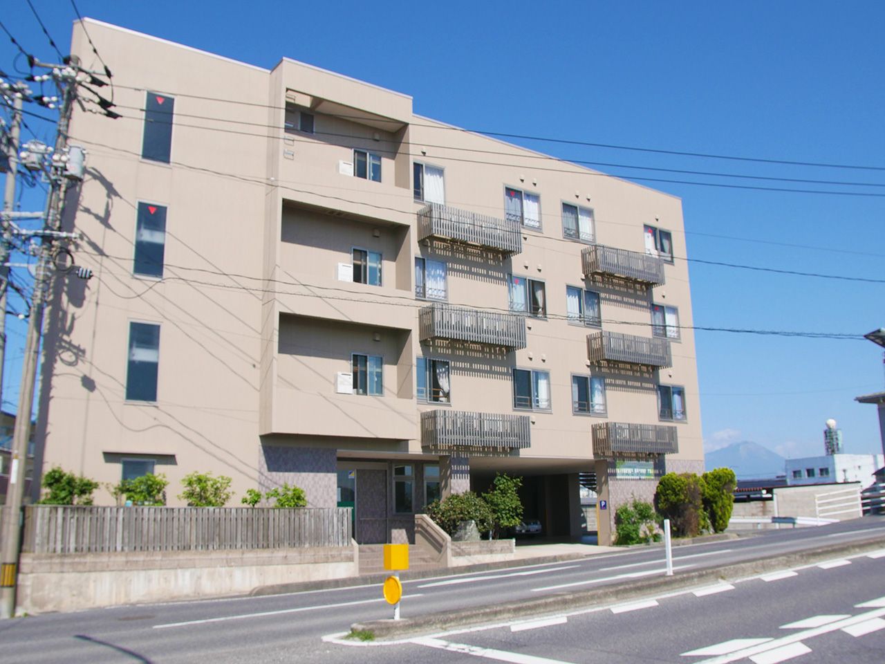 白を基調とした4階建ての建物は日当たりのいい場所に建っていて、建物の周りには草木が植えられている。