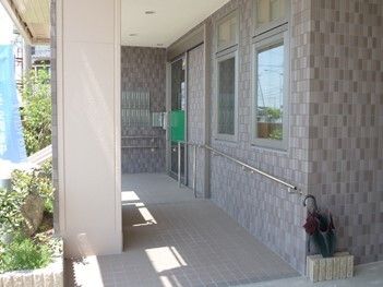 グレー系の外壁の建物の玄関は少し奥にあり、手すり付きのスロープが付いている。