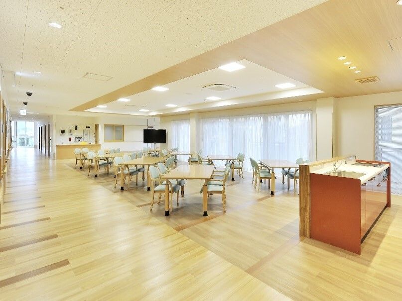 キッチンが付いたダイニングルーム。木製のテーブルが複数あり、大型のテレビも置かれている。