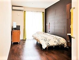 濃い色合いのフローリングと壁が印象的な部屋の様子。ベッドと日用品が置いてある様子