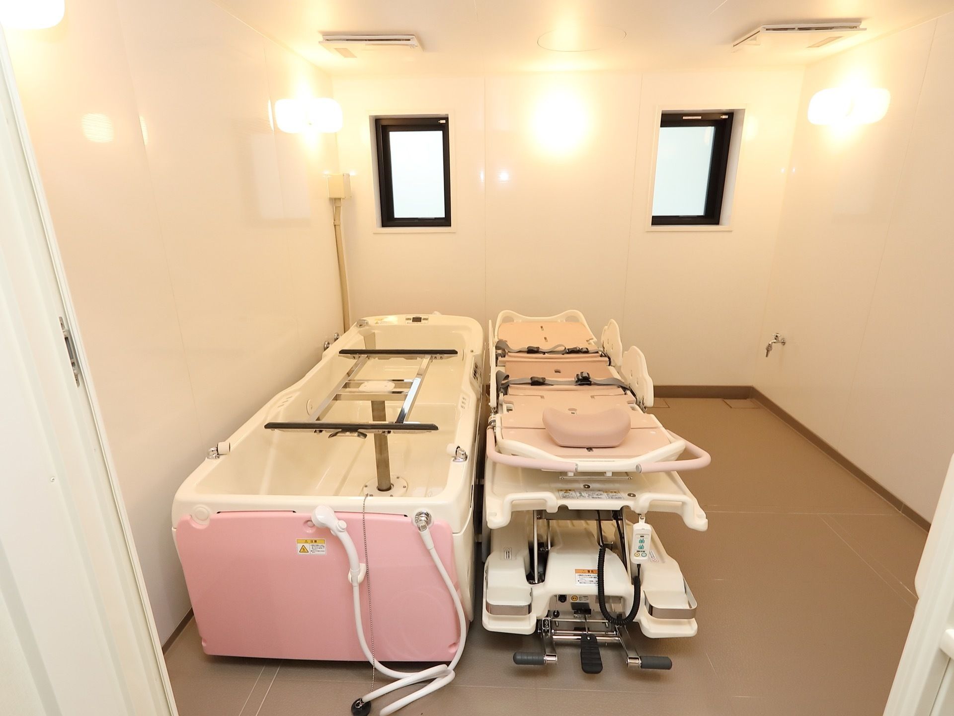 白い壁に茶色の床で、照明が暖色であたたかみのある浴室である。機械浴槽が置いてあり、寝たきりの状態の方でも入浴することができる。