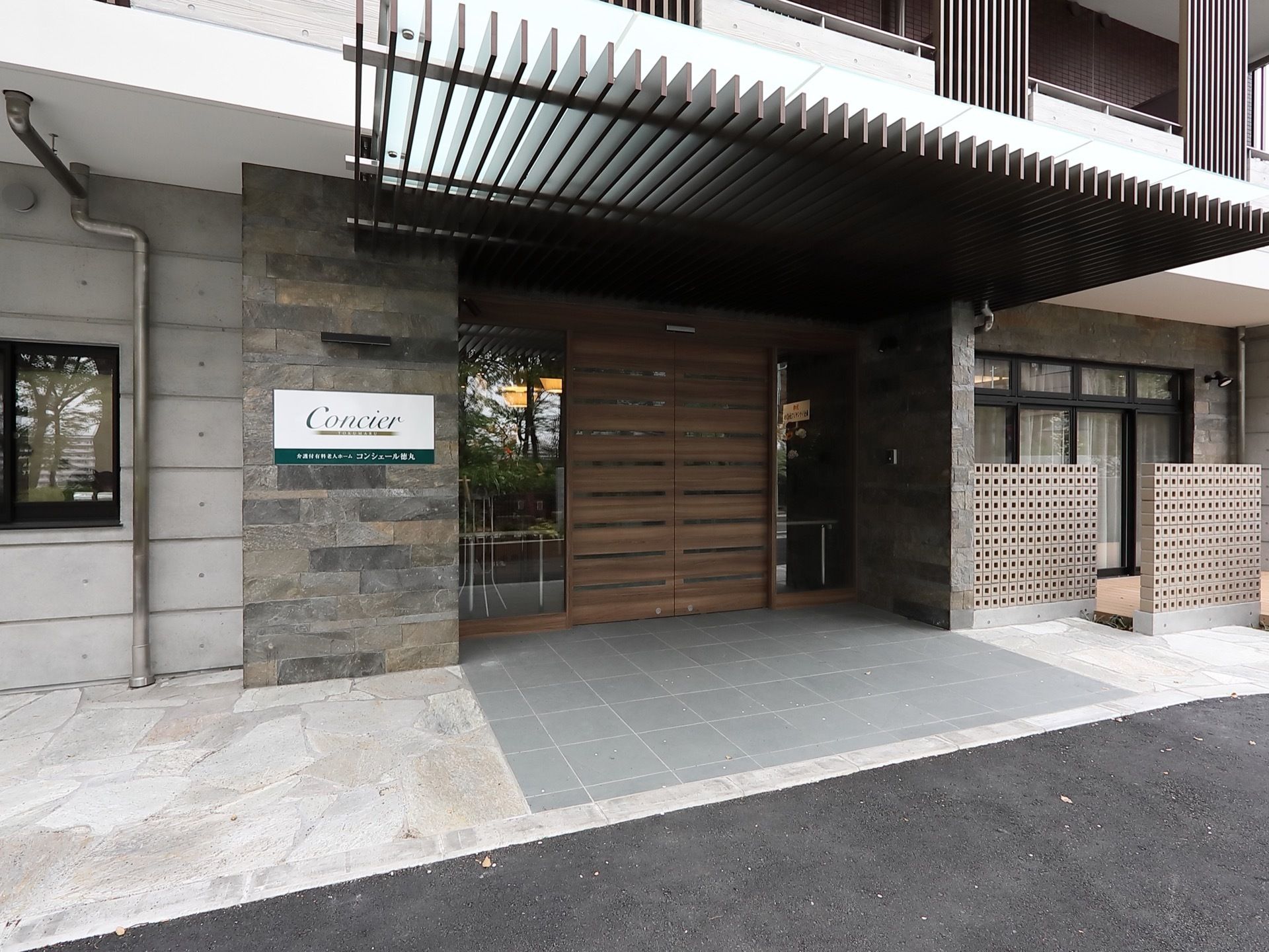 壁と地面の一部に天然石が使われている、落ち着いた雰囲気の玄関がある。扉は趣のある木製の両開きで、地面には段差がなく歩きやすくなっている。