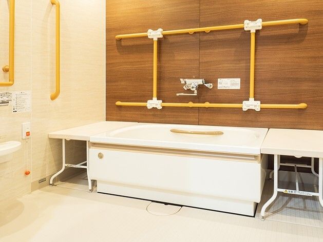 縦横に手すりが付いた浴室には一人用の浴槽が設置され、浴槽の両サイドにはベンチがあり、壁にはオレンジの呼び出しボタンもある。