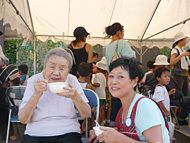 テントの下で食事を楽しむ入居者とエプロン姿の女性。