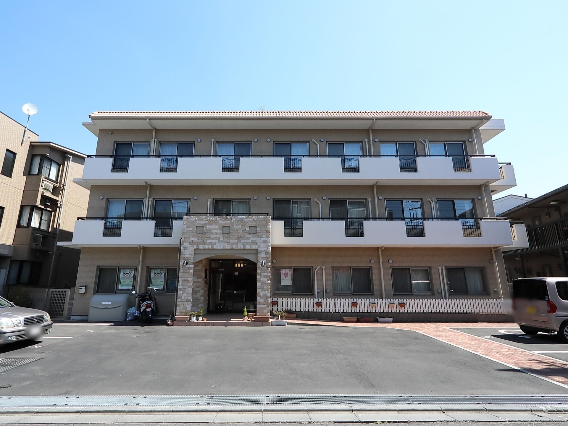 茶色と白の壁で構成された建物で、モザイク柄の玄関ポーチがせり出している。施設の前は駐車場になっている。