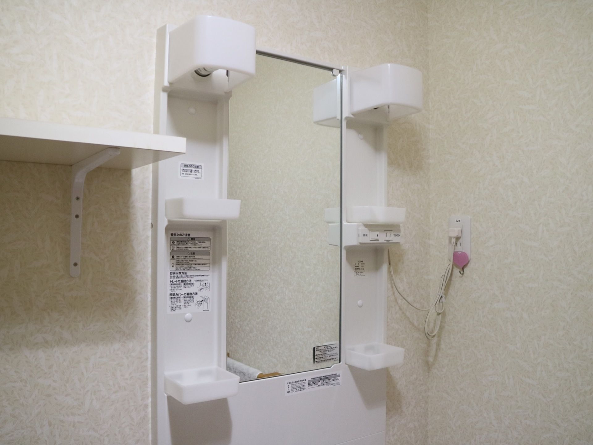 白を基調とした洗面台で、鏡の両サイドには収納棚が取り付けられている。他にも、照明やコンセントが設置されている。