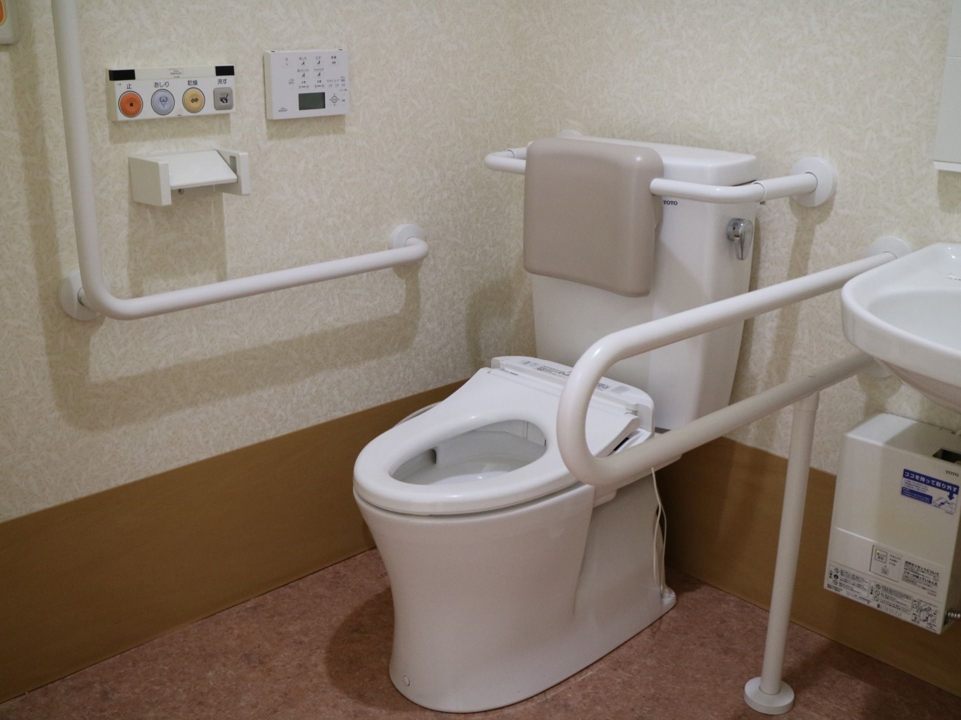 手洗い場が設けられている個室トイレ。便器横の壁には、操作パネルやＬ字型の手すりが取り付けられている。