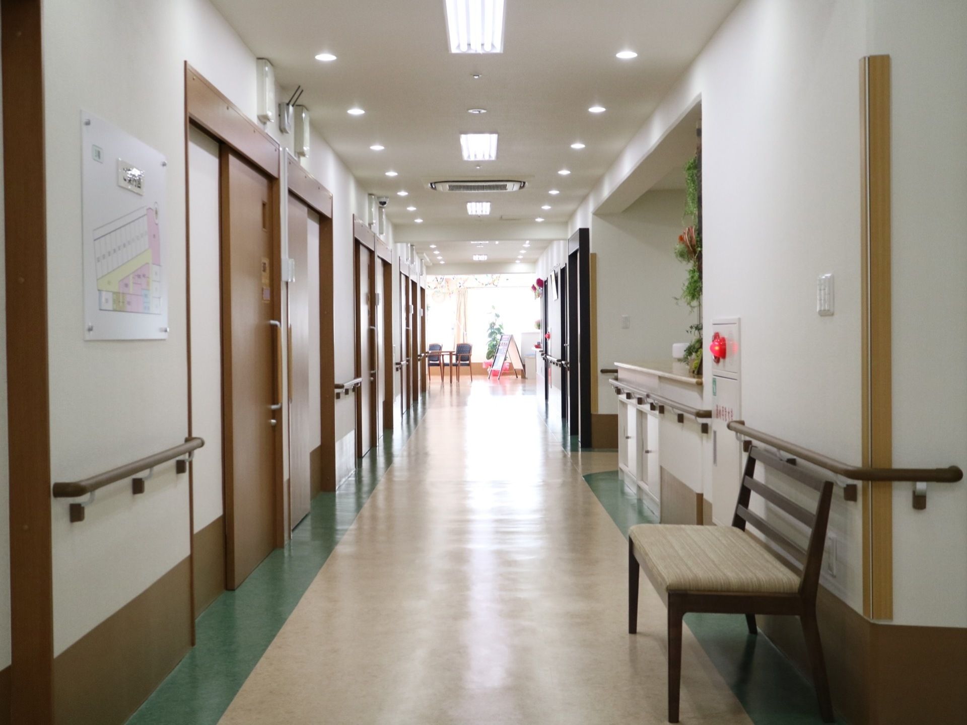 天井に蛍光灯や丸い複数の照明がある廊下で、手前にはベンチが置かれている。壁にはフロアの案内図が設置されている。
