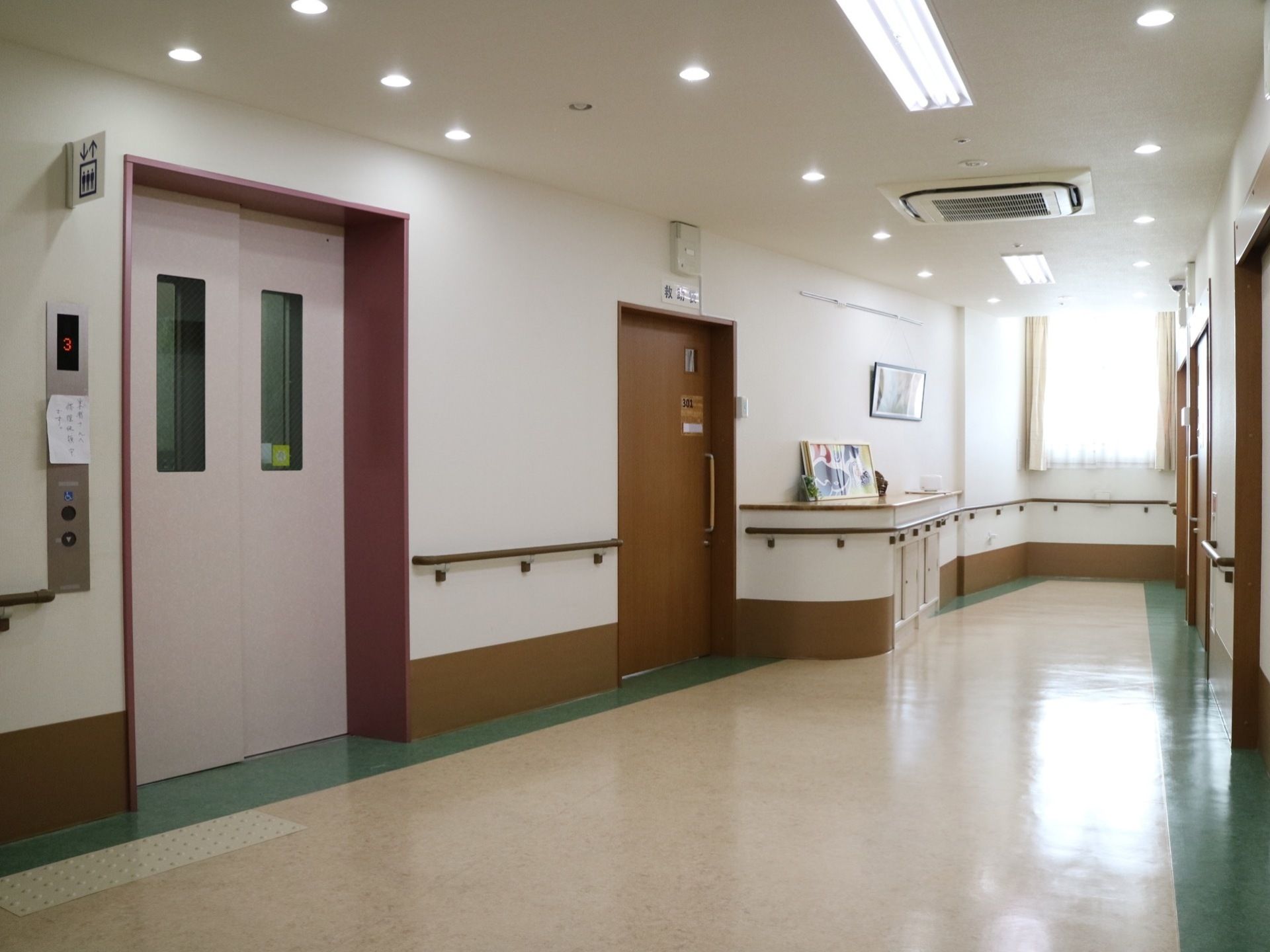 ピンク色の扉のエレベーターが１台設置されている。行先ボタンは、車椅子をご利用の方も押しやすいデザインとなっている。