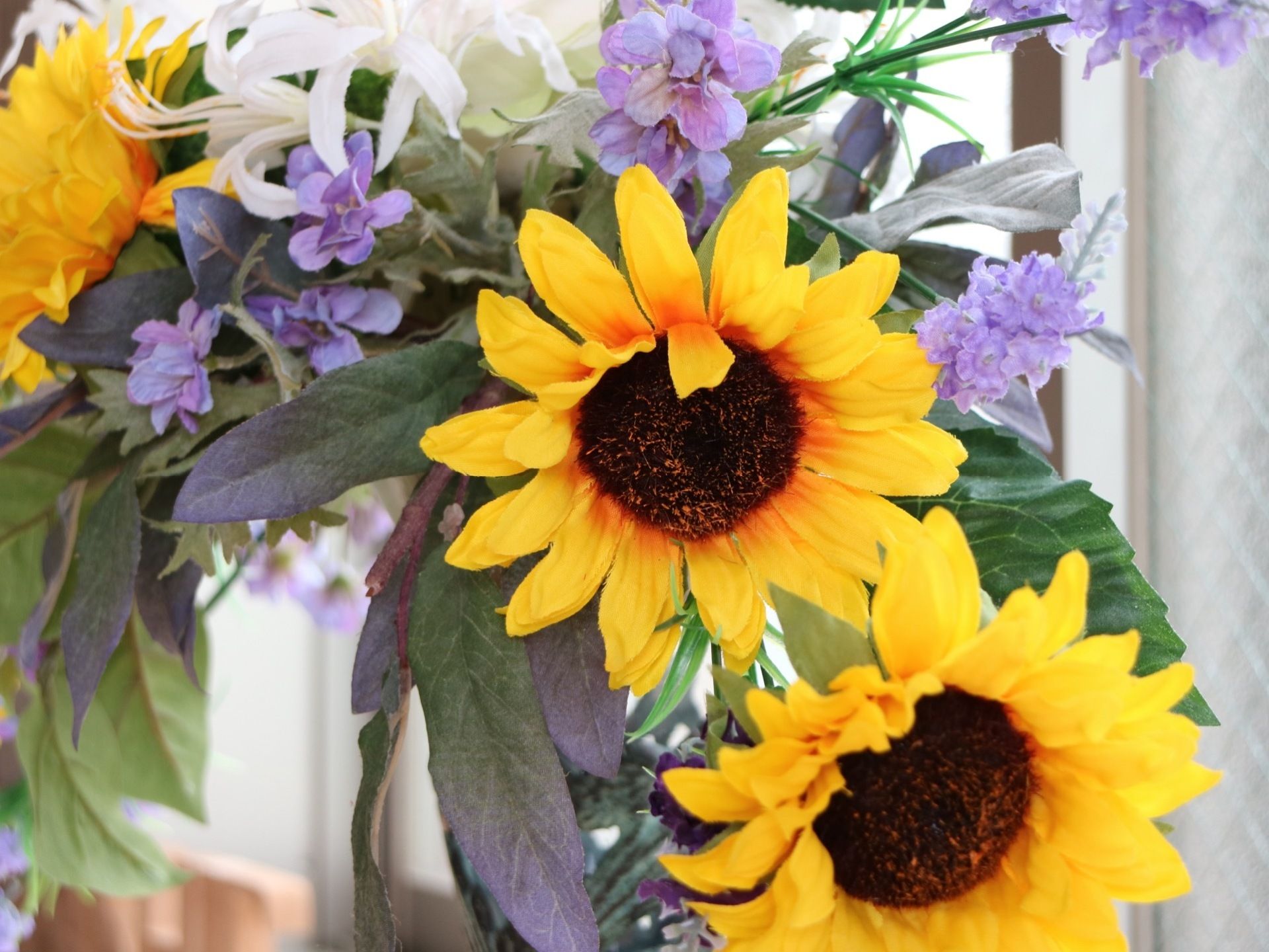 館内に設けられている明るいフロアに、花が装飾られている。複数のひまわりや紫色の花、白い花が飾られている。