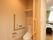 居室入口近くにある引き戸を開けるとトイレがある。天井に換気扇とダウンライトが設置されている。水洗のボタンが壁に取り付けられている。