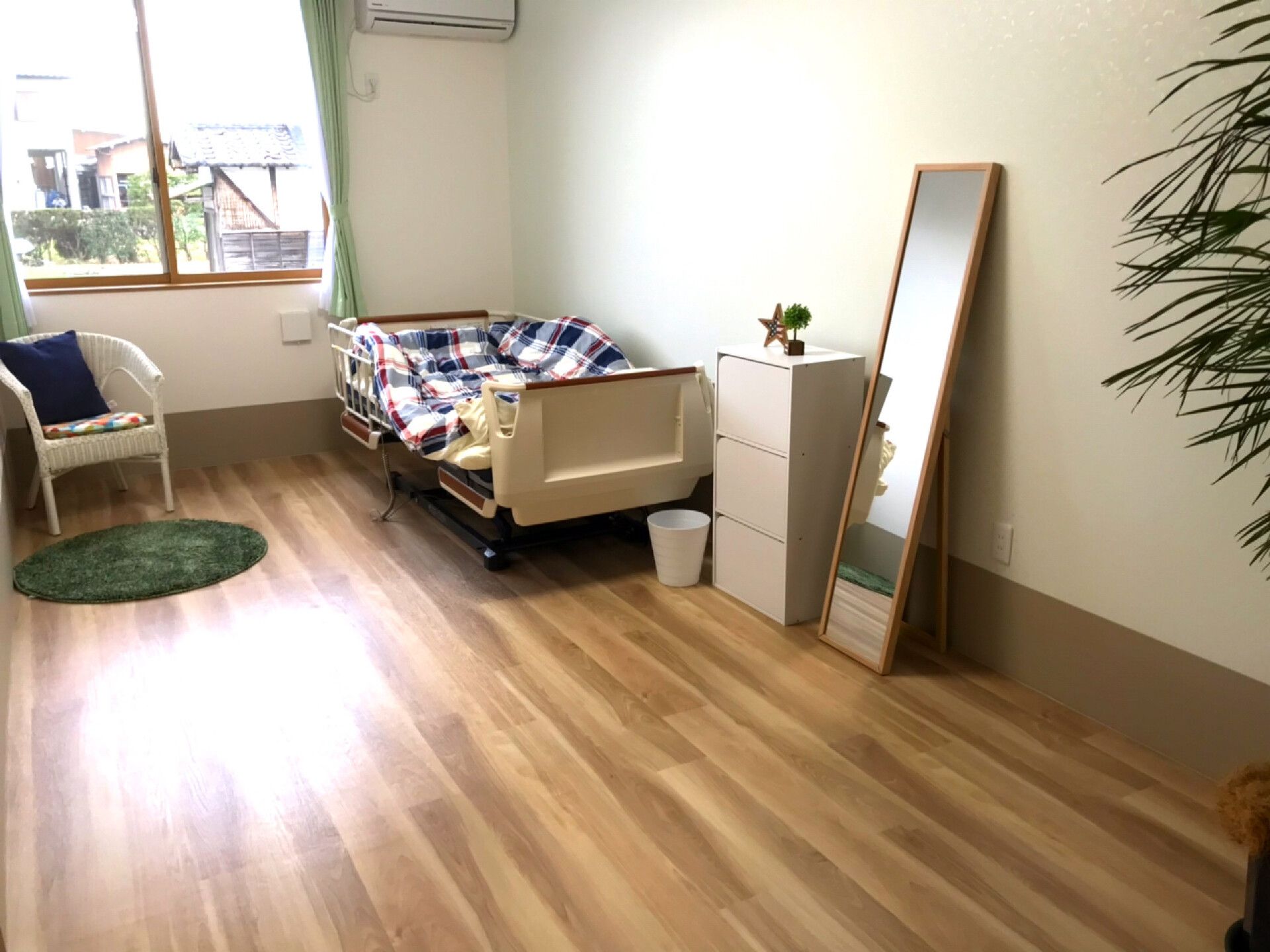 ブラウンのフローリングの部屋には寝具付きのベッドやテーブルセット、小さなチェストが置かれ、観葉植物が飾られている。窓が付き明るい雰囲気。