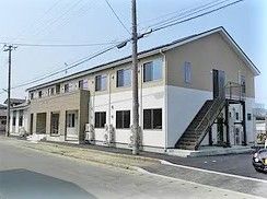 2階建ての建物を側面から見た様子。屋外に避難用階段が付き、玄関には階段だけでなくスロープも設置されている。