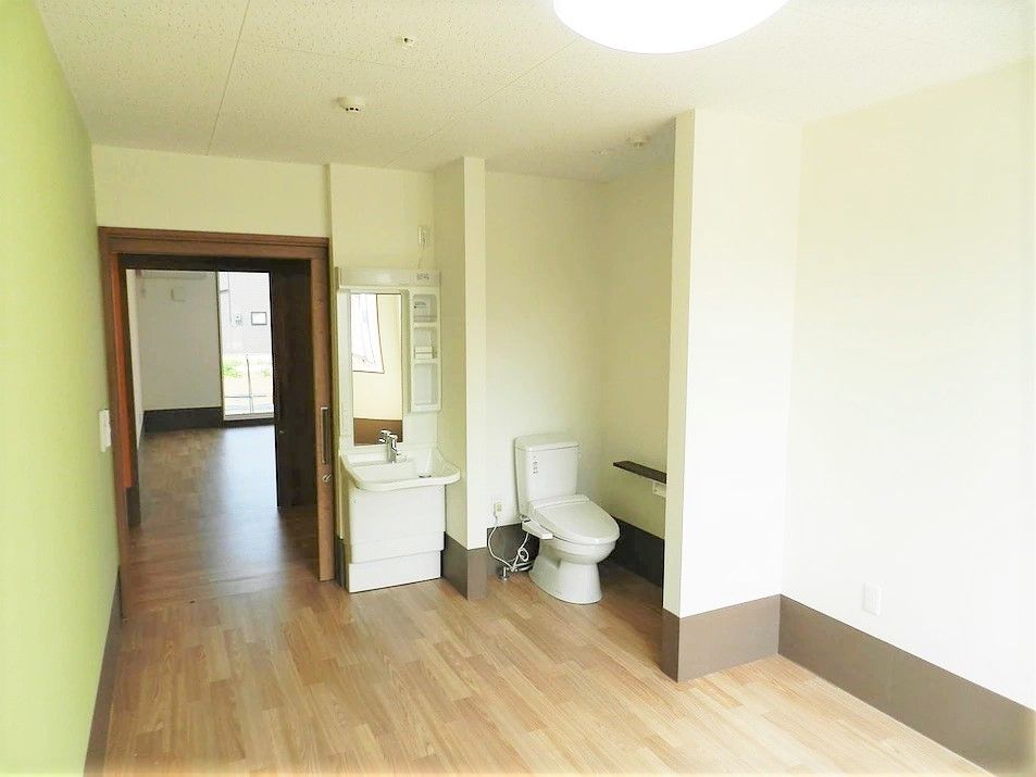 居室を入ると洗面所やトイレがあり、トイレにはドアがない。全体的に白い壁だが、右側の一面だけ鶯色。