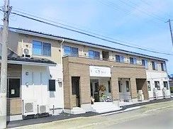 2階建ての建物を左斜め前方見た様子。玄関前には屋根が付き、道路に面している。