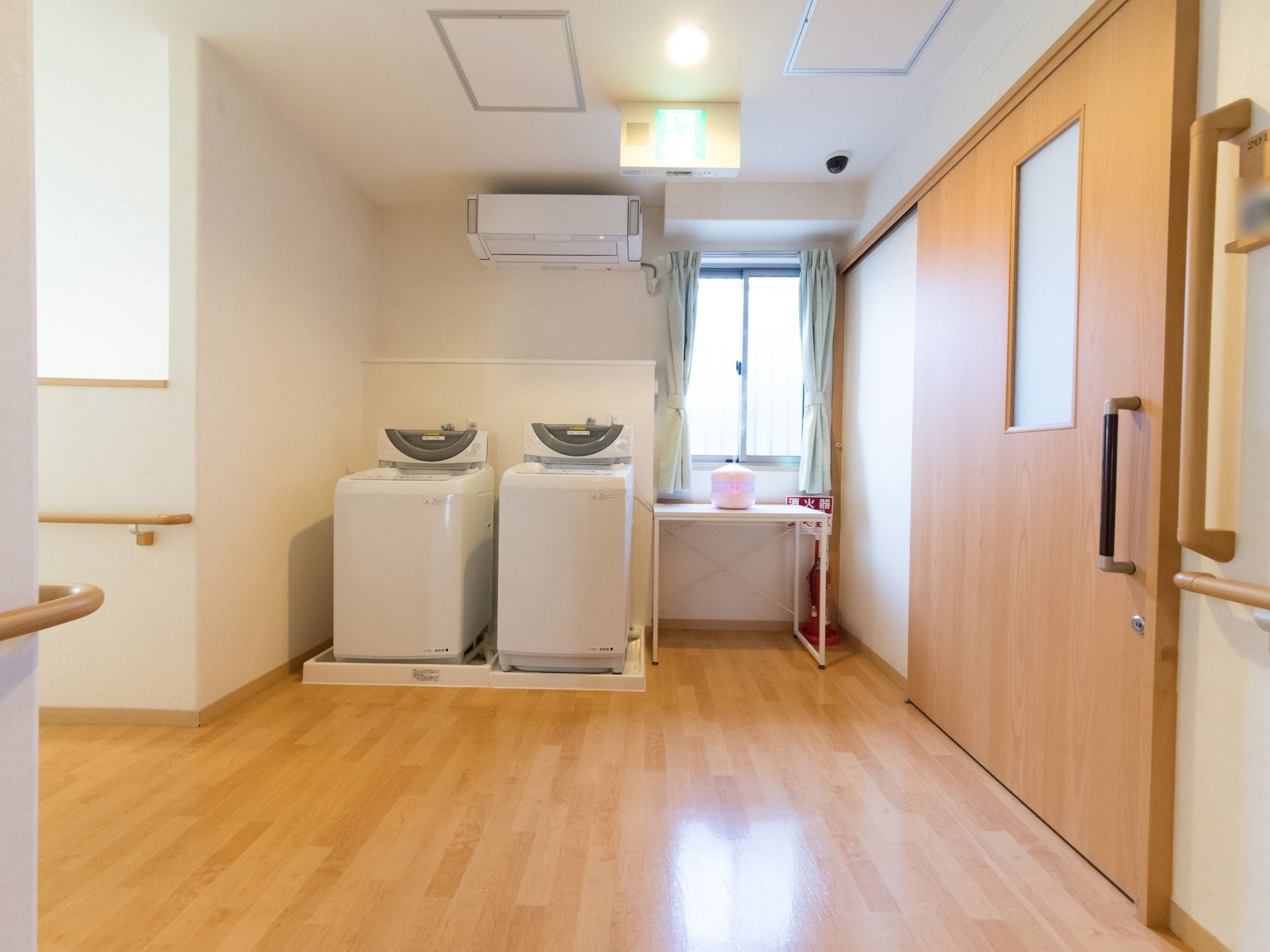 全自動洗濯機が２台備えられている。作業がし易いようにスペースは広く、隣に簡易テーブルと消火器が置いてある。