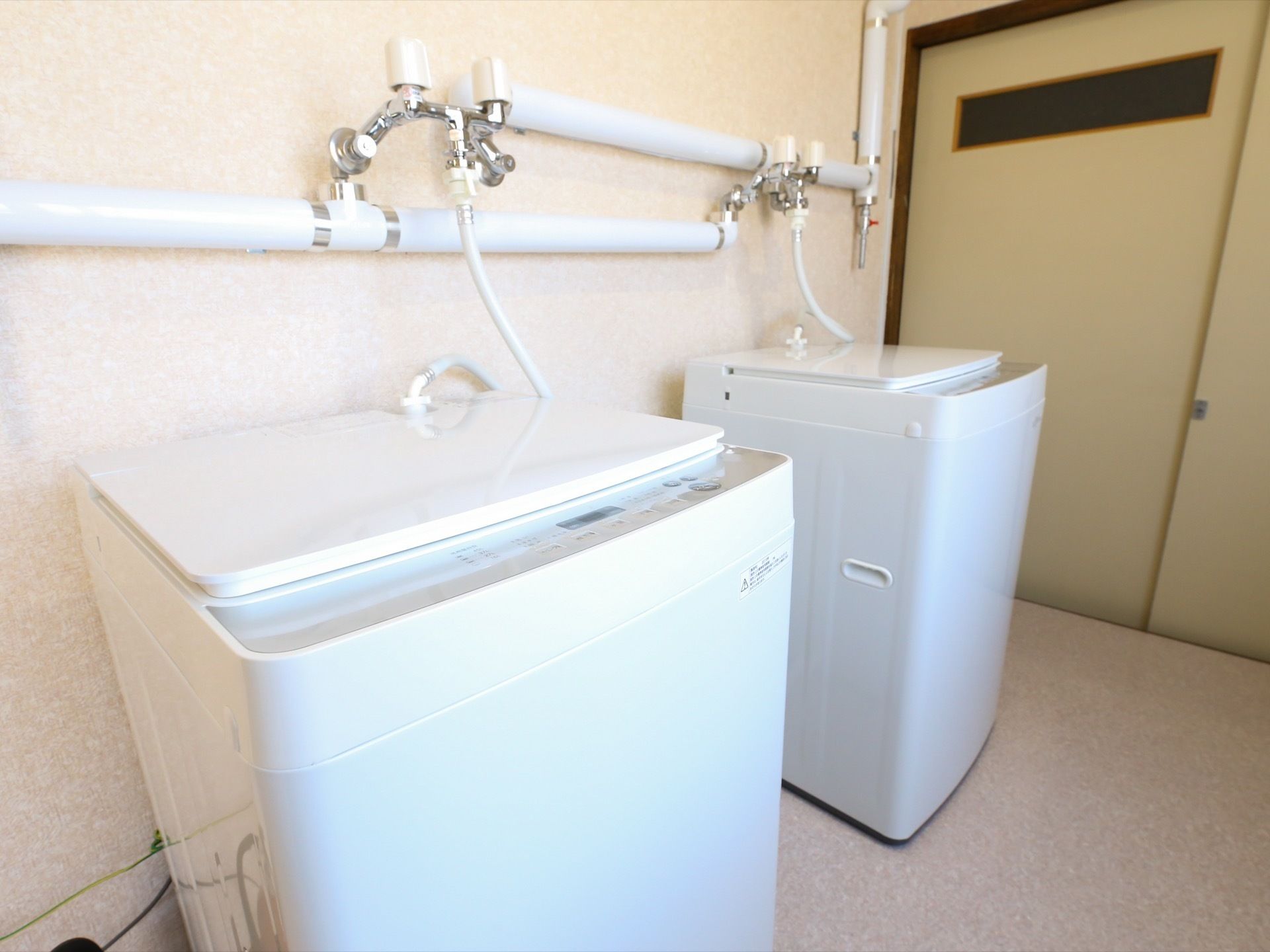 スライド式のクリーム色の扉が設置された洗濯室の壁際には、白い全自動洗濯機が2台並べられて置かれている。