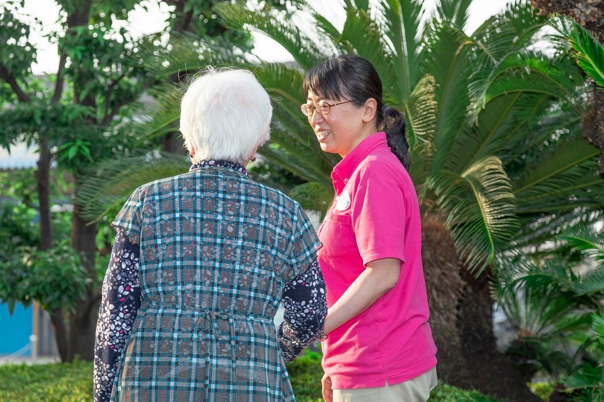 笑顔でこちらを向いている施設のスタッフと車いすに乗っている高齢者の様子。施設で写された写真